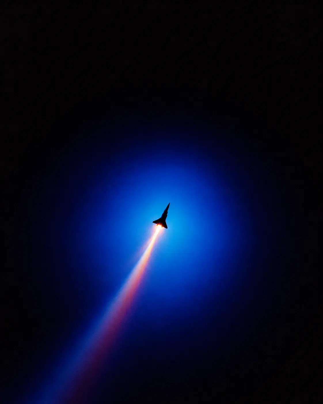 A tiny futuristic aircraft floating near the center of an enormous black and electric-blue void, a soft circular halo of blue light surrounding it, faint luminous trail extending diagonally downward, intense white-orange glow at the aircraft's rear, vast empty black space above and around the subject, soft lens bloom, subtle chromatic aberration, analog grain, dreamy experimental photography, mysterious minimalist sci-fi aesthetic, 4:5. STYLE LOCK: surreal retro-futuristic aviation photography, extreme minimalism, enormous negative space, tiny subject against monumental scale, electric cobalt blue and deep indigo palette, black voids, luminous white cores, orange and magenta chromatic fringes, long-exposure light trails, smooth atmospheric gradients, heavy optical bloom, soft diffusion, slight chromatic aberration, subtle analog film grain, dreamy experimental photography, high contrast, abstract geometric perspective, no realistic environment, no text, no UI, no stars, cinematic composition