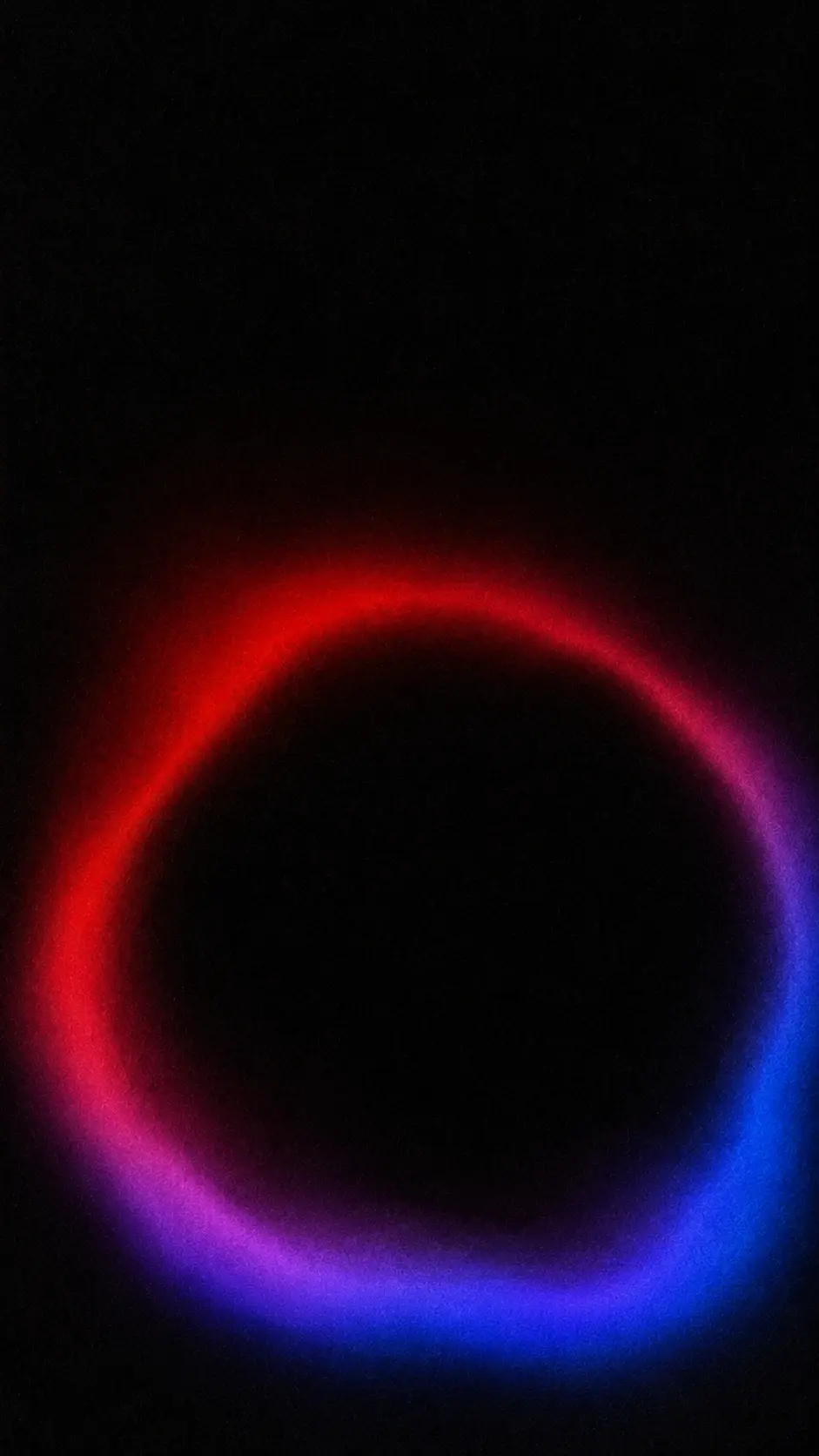 Abstract luminous color field, 9:16 portrait, completely black background, one oversized imperfect circular opening positioned low in the frame, thick soft organic perimeter with uneven thickness, deep scarlet and crimson transitioning into lavender, violet and electric blue, interior opening almost completely black, diffuse glowing edge, soft-focus photographic appearance, subtle chromatic bleeding, strong fine film grain, dusty analog texture, minimal mysterious composition, no geometric perfection, no text