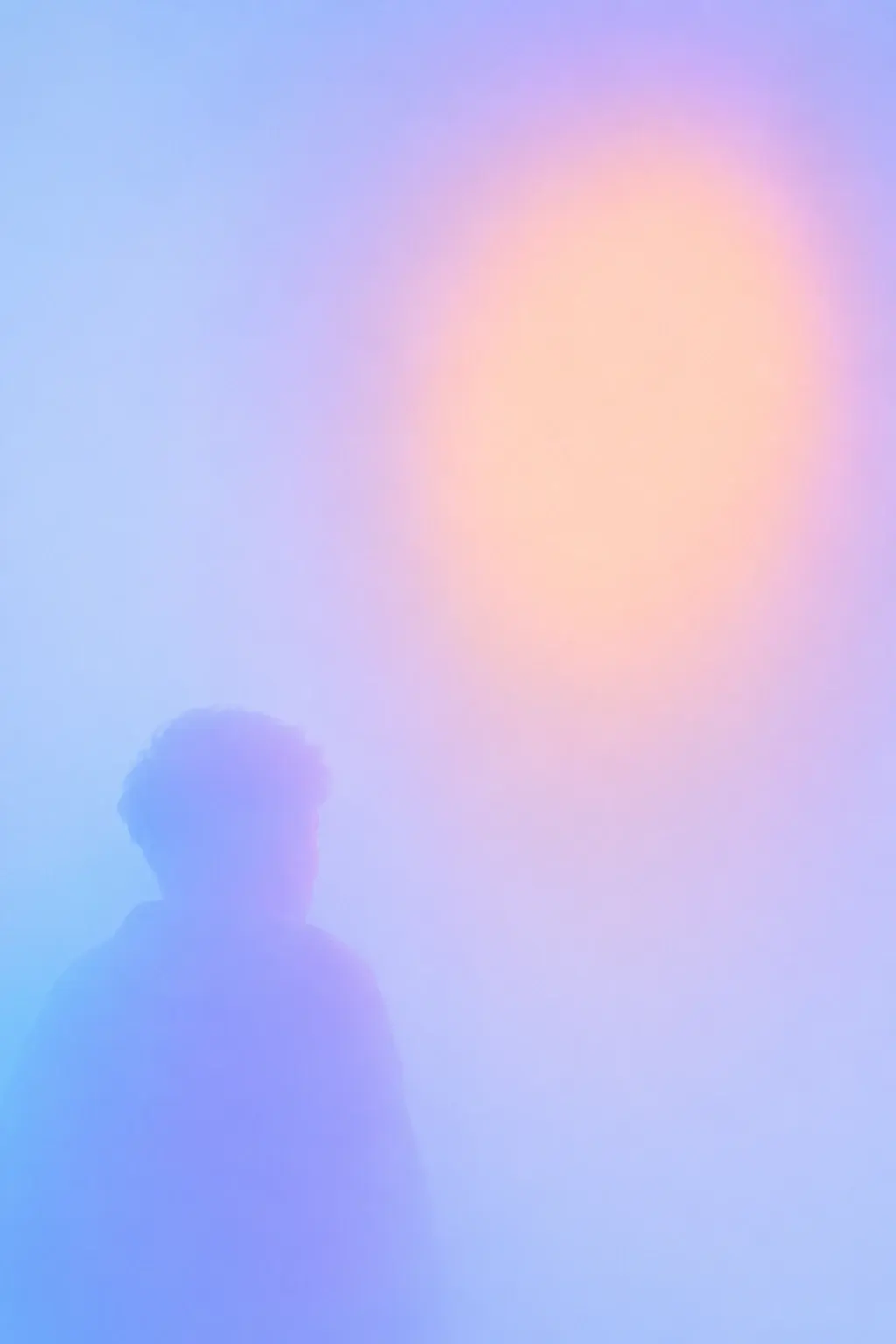 A large soft human silhouette occupying the lower-left portion of the frame, looking toward a huge irregular pale peach oval floating in the upper-right, the oval glowing through layers of blue and lavender haze, the person's silhouette fading into the background, extremely sparse composition with most of the frame empty. STYLE LOCK